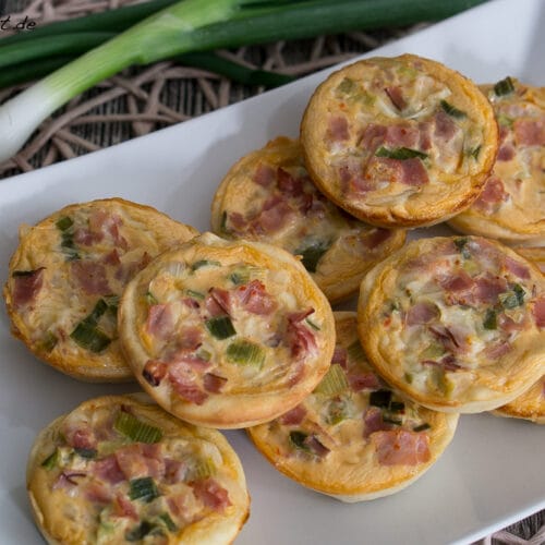Mini Quiches mit Schinken Rezept 3 Mini-Quiches, gefüllt mit Schinken und Lauchzwiebeln auf einem Teller.