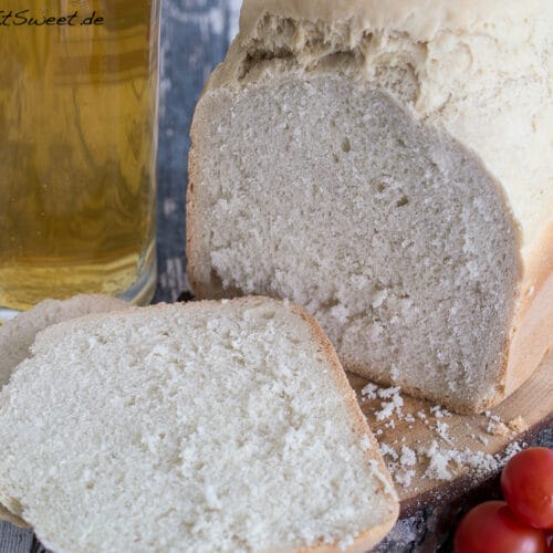 Weißes Bierbrot aus dem Brotbackautomat mit zwei Scheiben und einem Glas Bier auf einem Holztisch.