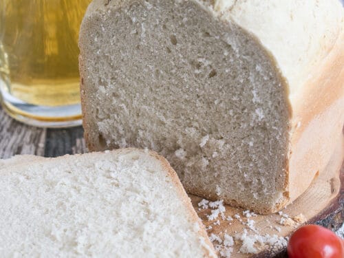 Hausgemachtes Bierbrot mit einer Scheibe davor und einem Glas Bier im Hintergrund.