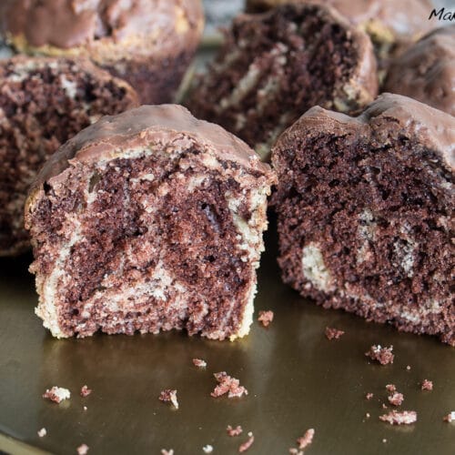 Marmorkuchen Muffins mit glänzender Oberfläche, die aufgeschnitten werden, um das gewirbelte Schokoladen- und Vanillemuster im Inneren zu zeigen.