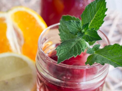 Ein Glas roter Sommer Eistee mit Minze, Orangen- und Zitronenscheiben.