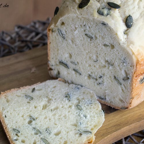 Kürbisbrot mit Joghurt und Kürbiskernen, eine Scheibe geschnitten, auf einem Holzbrett ausgestellt.
