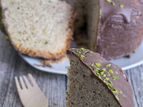 Ein Stück Mandelkuchen mit Schokolade mit Schokoladenglasur und gehackten Pistazien obenauf.