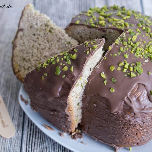 Mandelkuchen mit Schokolade und Pistazien - Kuchen Brotbackautomat 3 Mandelkuchen aus dem Brotbackautomat mit Schokolade und gehackten Pistazien, zwei Stücke herausgeschnitten, auf einem Teller und einer Holzgabel daneben.
