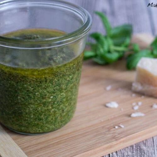 Basilikum Pesto selber machen 3 Glasgefäß mit grünem Basilikum Pesto selbst machen mit frischen Basilikumblättern und einem Stück Parmesankäse daneben.