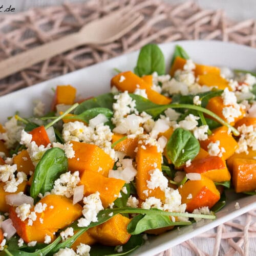 Kürbissalat mit Spinat und Feta Rezept 3 Kürbissalat mit Spinat mit geröstetem Kürbis, Feta und Zwiebeln auf einem rechteckigen weißen Teller.