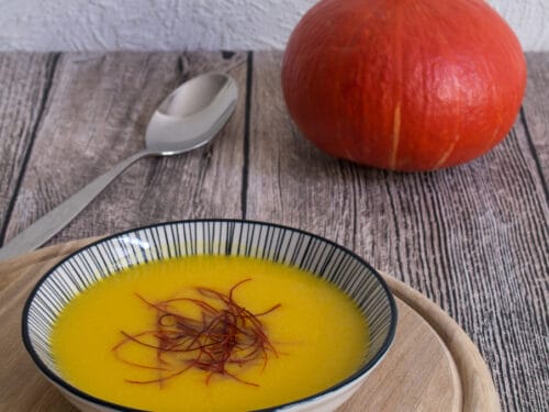 Schale mit einfacher Kürbissuppe auf einem Holzbrett.