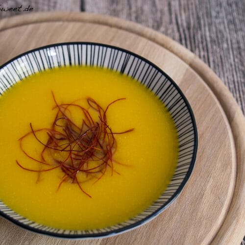 Schale mit leuchtend gelber einfacher Kürbissuppe, die mit Safranfäden verziert ist.