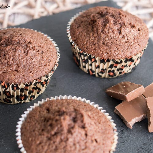 Drei Schokomuffins und Stücke Milchschokolade auf Schieferplatte.