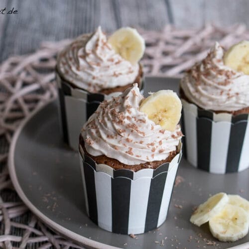 Muffin mit Nutella Füllung und Bananen-Topping 3 Drei Schoko-Nuss-Muffins mit Bananen-Topping, Bananenscheiben und Schokoladenraspeln auf einem Teller.