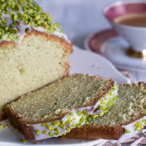 Geschnittener Avocado-Kuchen mit Mandeln, einer weißer Glasur und gehackten Pistazien, zu einer Tasse Kaffee.