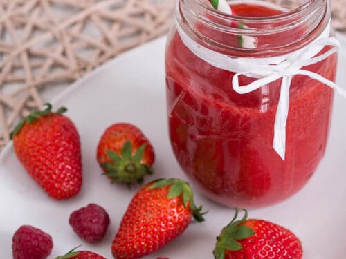 Einmachglas mit Erdbeer-Smoothie mit Himbeeren und einem gestreiften Strohhalm, umgeben von Erdbeeren und Himbeeren auf einem Teller.