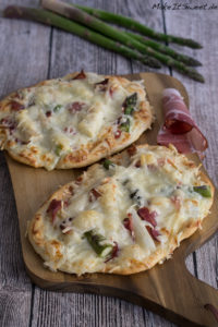Flammkuchen mit Spargel und Schinken 2 Zwei Flammkuchen mit geschmolzenem Käse, Schinken und frischem Spargel auf einem Holzbrett.