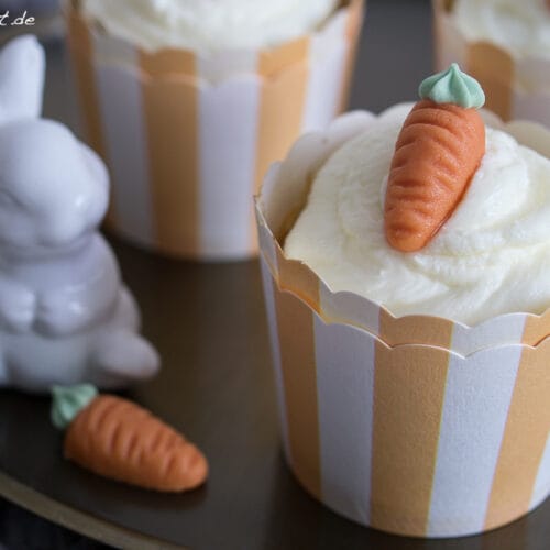 Karottenmuffins mit Mandeln und Frischkäse Topping 3 Karottenmuffins mit Mandeln, weißem Frosting und Karottendekor.