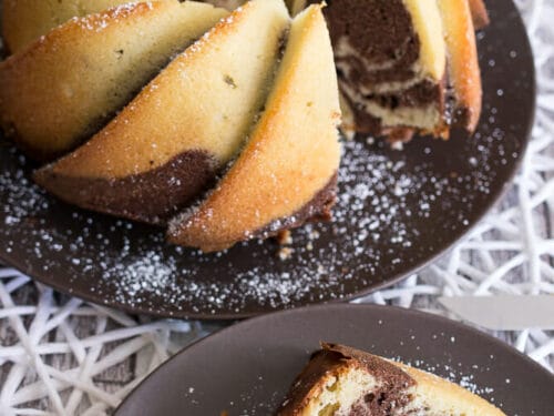 Marmorkuchen mit Schokoladen- und Vanillestrudel, bestreut mit Puderzucker, serviert auf dunklen Tellern.