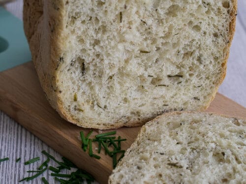 Hausgemachtes Brot mit Schnittlauch, eine Scheibe geschnitten, mit frischem Schnittlauch bestreut, auf einem Holzbrett.
