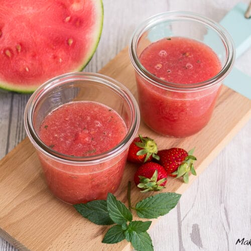 Wassermelone-Erdbeere-Limonade mit Minze 3 Zwei Gläser mit Wassermelonen-Erbeeren-Limonade mit Minze und einer Wassermelonenscheibe auf einem Holzbrett.