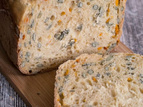 Kürbisbrot mit Chili und Kürbiskernen mit einer aufgeschnittenen Scheibe, die Samen und rote Chilischoten als Zutaten zeigt.