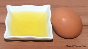 Braunes Ei und eine Schale mit Eiweiß auf Holz.