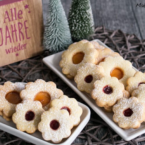 Blumenförmige Hildabrötchen mit Marmeladenkern und Puderzucker auf Tellern.