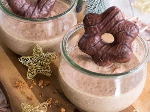 Zwei Gläser Lebkuchenpudding-Schokoladenmousse mit Lebkuchen auf einem Holzbrett.
