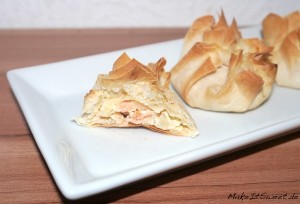 Lachstaschen mit cremiger Füllung, eine aufgeschnitten auf einem weißen Teller, dahinter weiteres Gebäck.