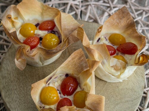 Drei Muffins aus Filoteig, gefüllt mit cremigem Feta, roten und gelben Kirschtomaten, dicht aneinander gereiht.