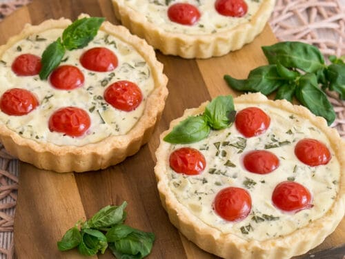 Drei herzhafte Mini-Tartelettes, belegt mit Kirschtomaten und Basilikum.