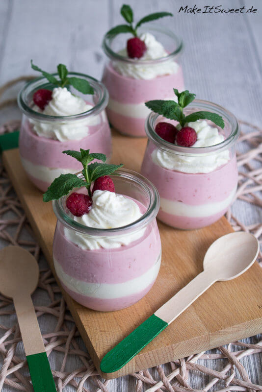 Himbeerquark mit Sahne in einem Glas geschichtet. Mit Himbeeren und Minze als Dekoration