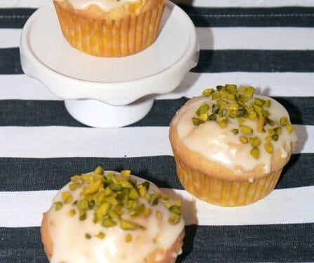 Drei Mango-Maracuja-Muffins mit weißer Glasur und gehackten Pistazien oben drauf.