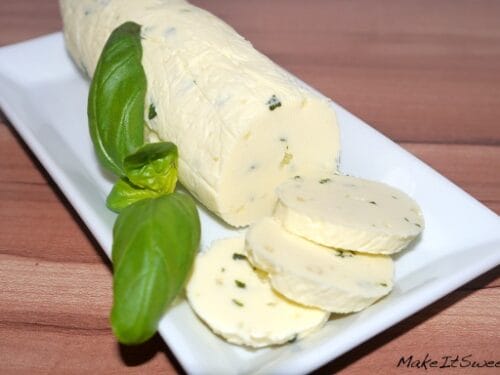 Kräuterbutter mit Knoblauch und Basilikum, teilweise aufgeschnitten, auf einem weißen, rechteckigen Teller präsentiert.