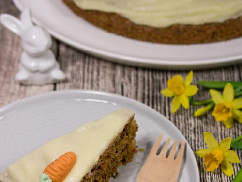Ein Stück Karottenkuchen mit Walnüssen und Butterglasur wird vor dem Rest der Torte angerichtet.