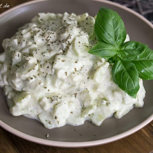 Cremiger Gurkensalat mit Schmand und Gurkenscheiben auf einem braunen Teller.