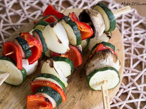 Gegrillte Gemüsespieße mit Zucchini, Zwiebel, roter Paprika und Champignons auf einem Holzbrett.