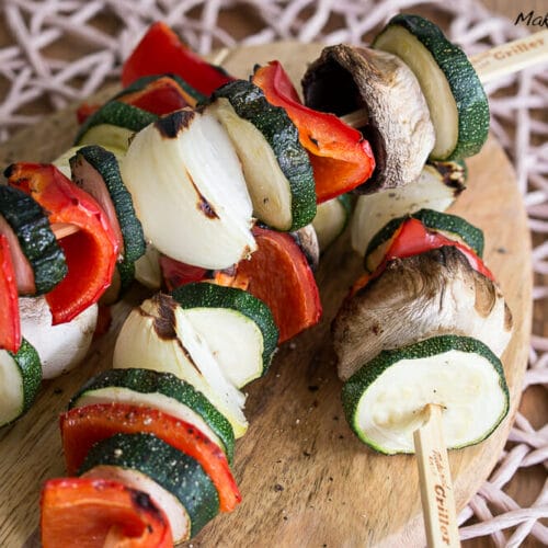 Gemüsespieße vom Grill 3 Gegrillte Gemüsespieße mit Zucchini, Zwiebel, roter Paprika und Champignons auf einem Holzbrett.