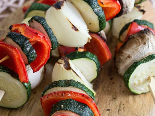 Gegrillte Gemüsespieße mit Zucchini, roter Paprika, Zwiebel und Champignon auf einem Holzbrett.