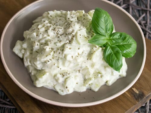 Cremiger Gurkensalat mit Schmand, Gurkenscheiben und Dill, serviert in einer beigen Schale.