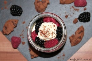 Ein Glas Schlagsahne mit Himbeeren, Brombeeren und Cookies auf einer Schieferplatte.