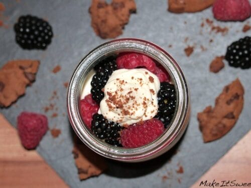 Ein Glas Schlagsahne mit Himbeeren, Brombeeren und Cookies auf einer Schieferplatte.