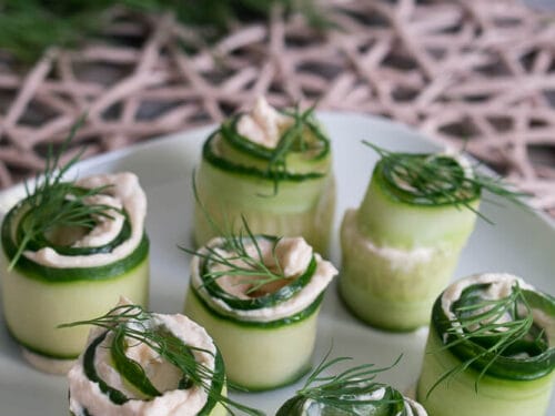 Gurken Röllchen mit Räucherlachs, Frischkäse und Dill-Garnitur auf einem weißen Teller.