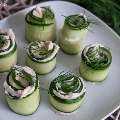 Mit Räucherlacs und Frischkäse gefüllte und mit Dill bestreute Gurken-Röllchen, hübsch angerichtet auf einem weißen Teller.