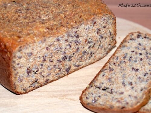 Teilweise aufgeschnittenes Low Carb Eiweißbrot mit Kernen liegt auf einem Schneidebrett aus Holz.