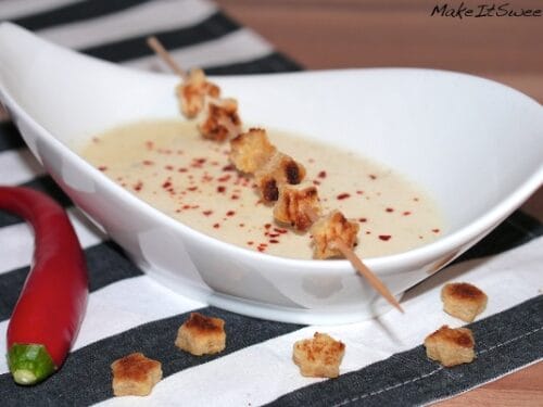 Schüssel mit cremiger Parmesanschaumsuppe, garniert mit einem Crouton-Spieß und Chiliflocken.