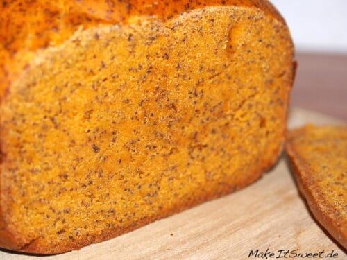 In Scheiben geschnittenes Tomaten-Mohn-Brot mit orangefarbener Krume und sichtbaren Kernen auf einer Holzunterlage.