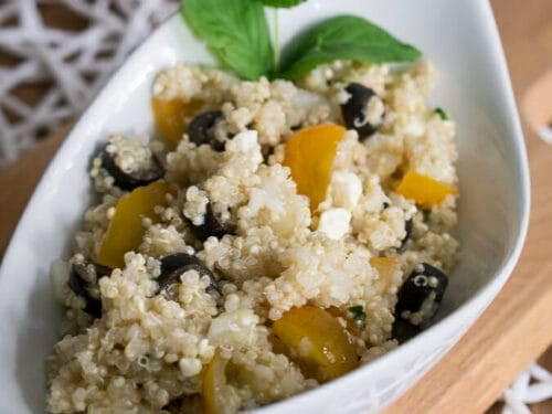 Griechischer Quinoa-Salat mit Feta, Tomate, schwarzen Oliven und Minze in weißer Schüssel.