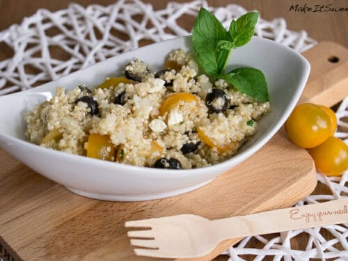 Quinoa-Salat mit Feta, gelben Tomaten, schwarzen Oliven und frischer Minze in einer weißen Schale.