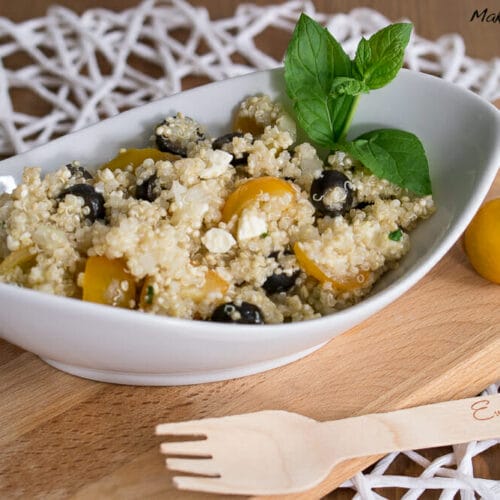 Griechischer Quinoa Salat mit Feta, Olive und Tomate 3 Quinoa-Salat mit Feta, gelben Tomaten, schwarzen Oliven und frischer Minze in einer weißen Schale.