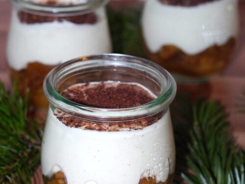 Drei Gläser Tiramisu mit Bratapfel, überzogen mit einer Creme und bestäubt mit Kakaopulver.