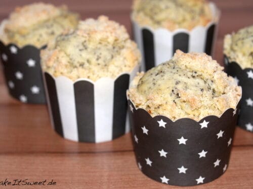 Vier Mohnmuffins mit Streuselfüllung in Papierförmchen.