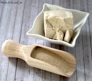 Frische Hefe in einer Schüssel und Trockenhefe in einer Holzkelle auf einer Holzunterlage, Zutaten für Hefeteig.